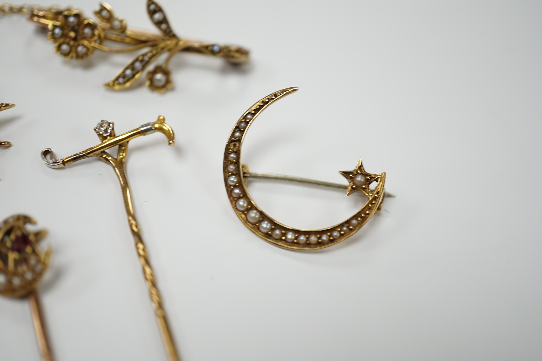 Three early to mid 20th century yellow metal and seed pearl set brooches, largest 34mm, two similar stick pins and a diamond set riding crop stick pin.